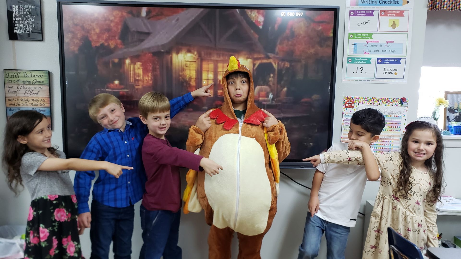 Children pointing at person in turkey costume in classroom.