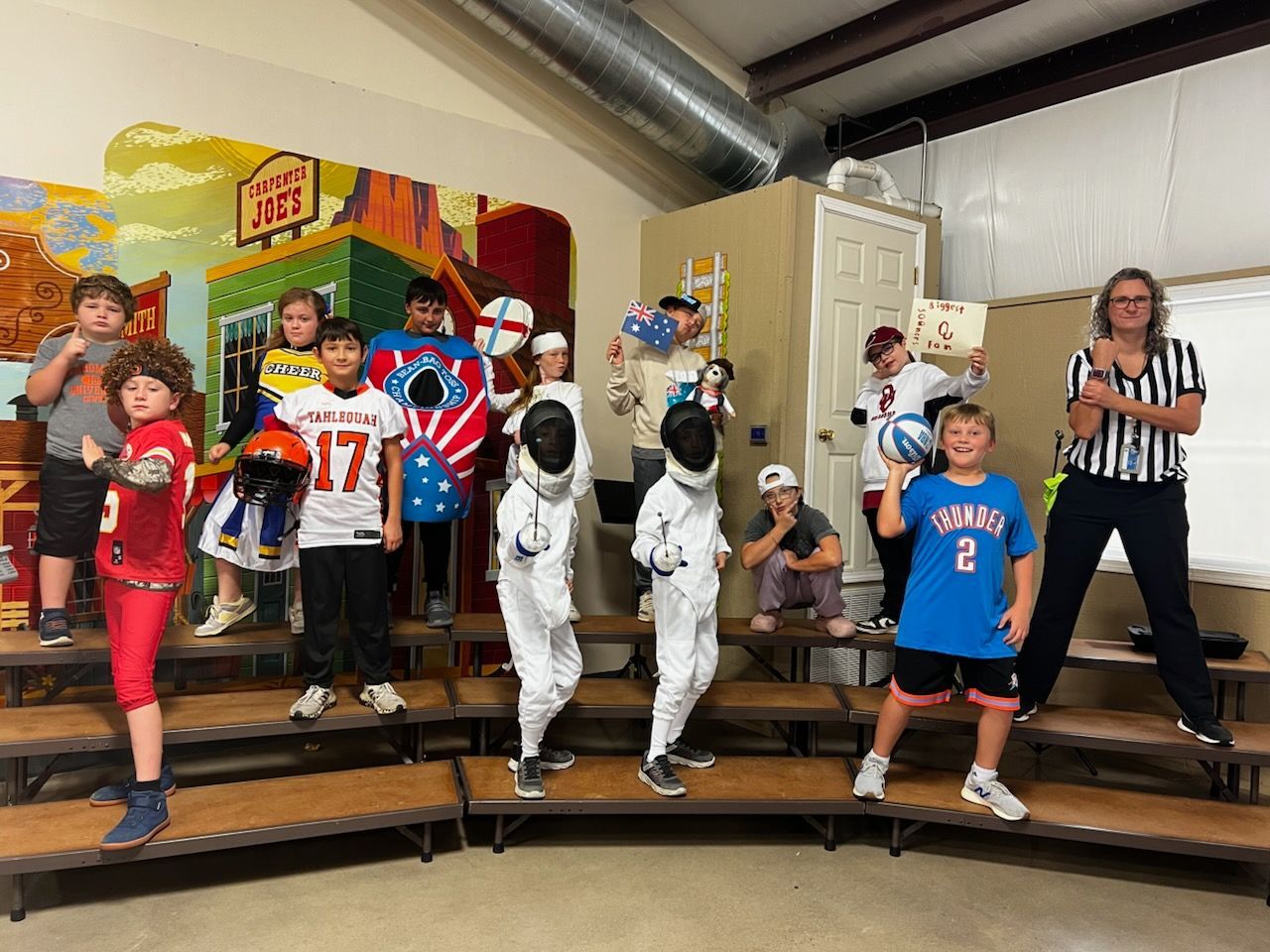 Children in costumes on risers, teacher. Stage backdrop: