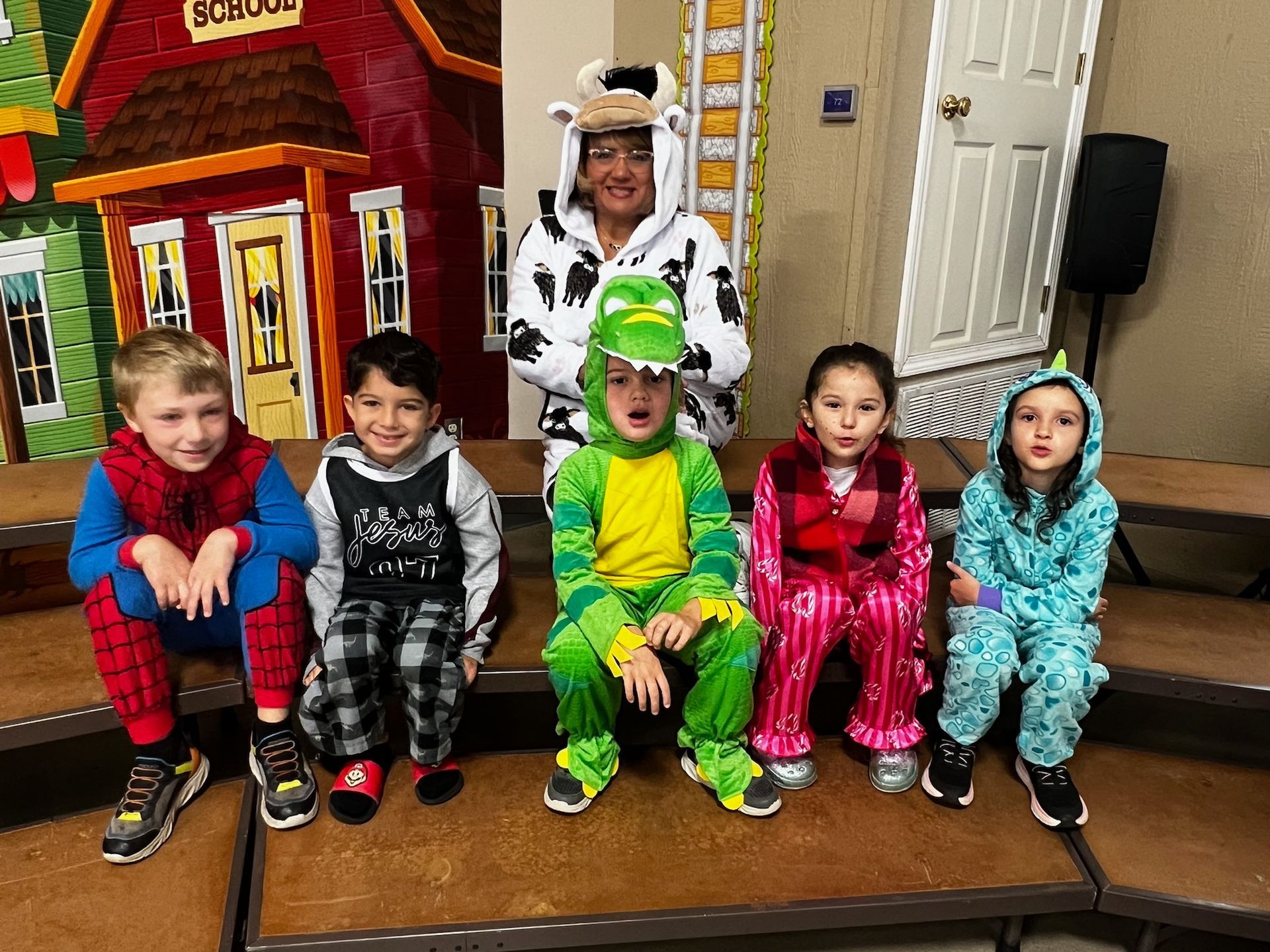 Children and an adult in costumes, sitting on steps with a school backdrop.