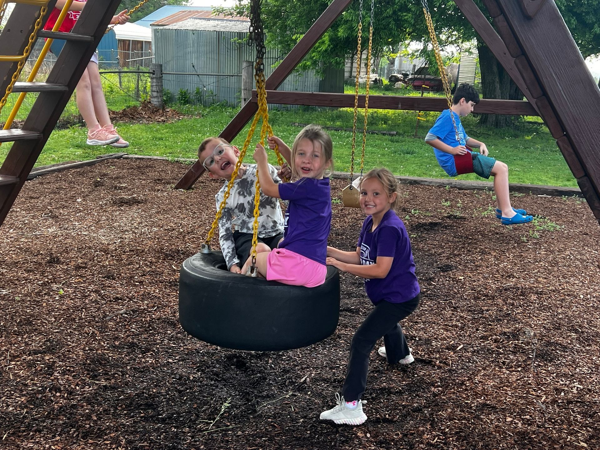 Children playing on a tire swing at a playground, with one girl pushing another.