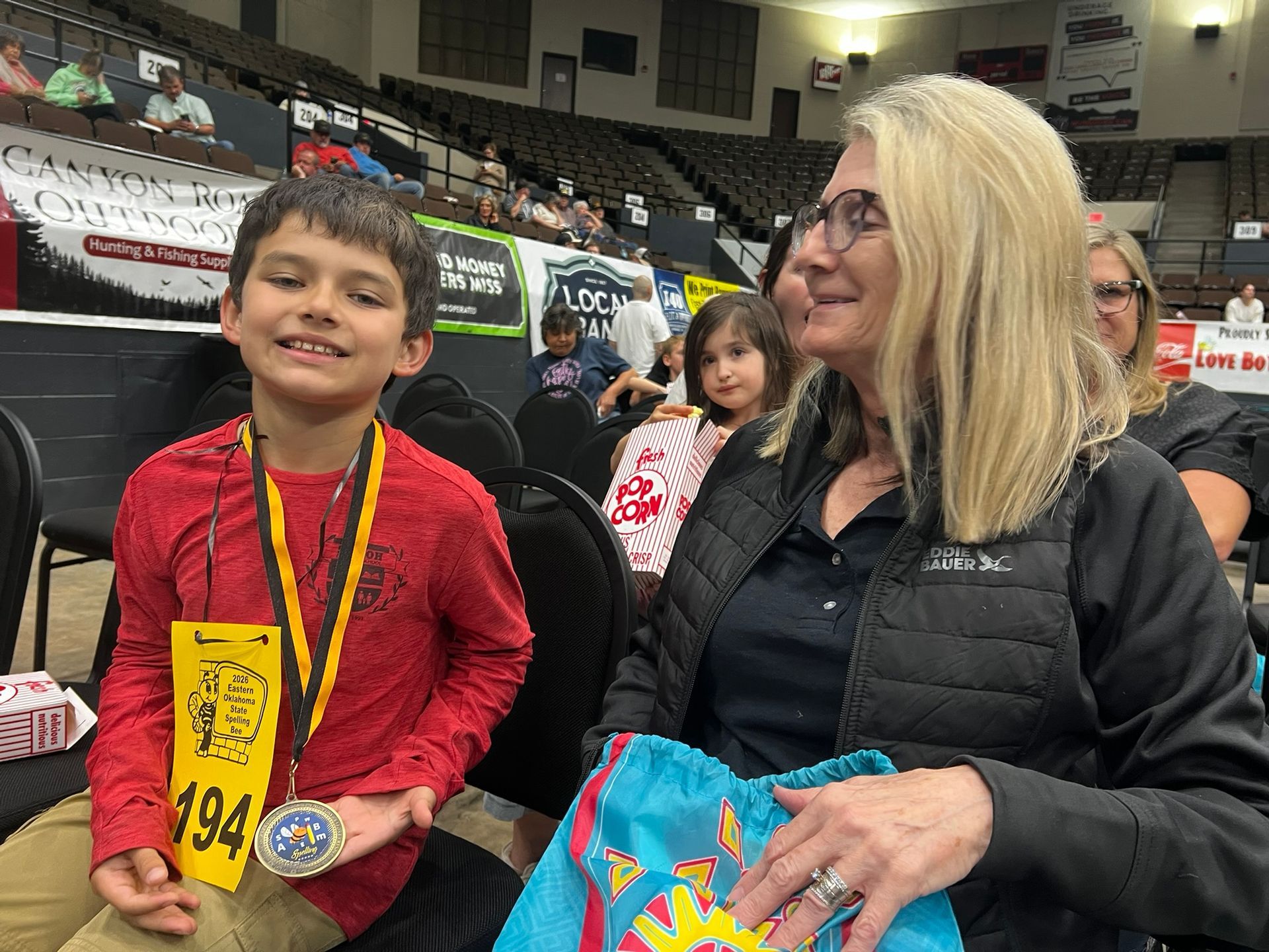 Boy with medal and woman holding a gift bag in an indoor sports arena.