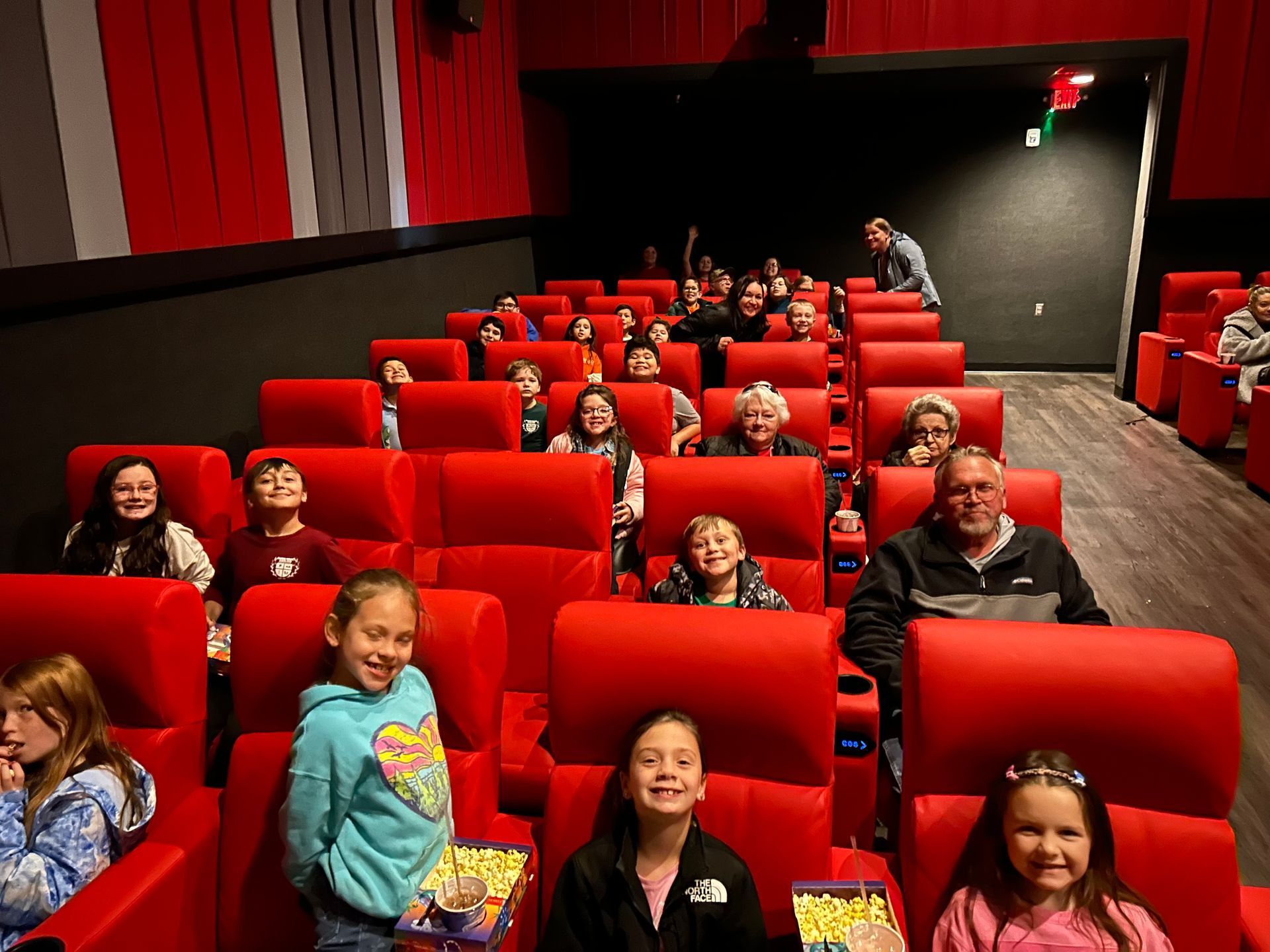 A group of people are sitting in red chairs in a movie theater.
