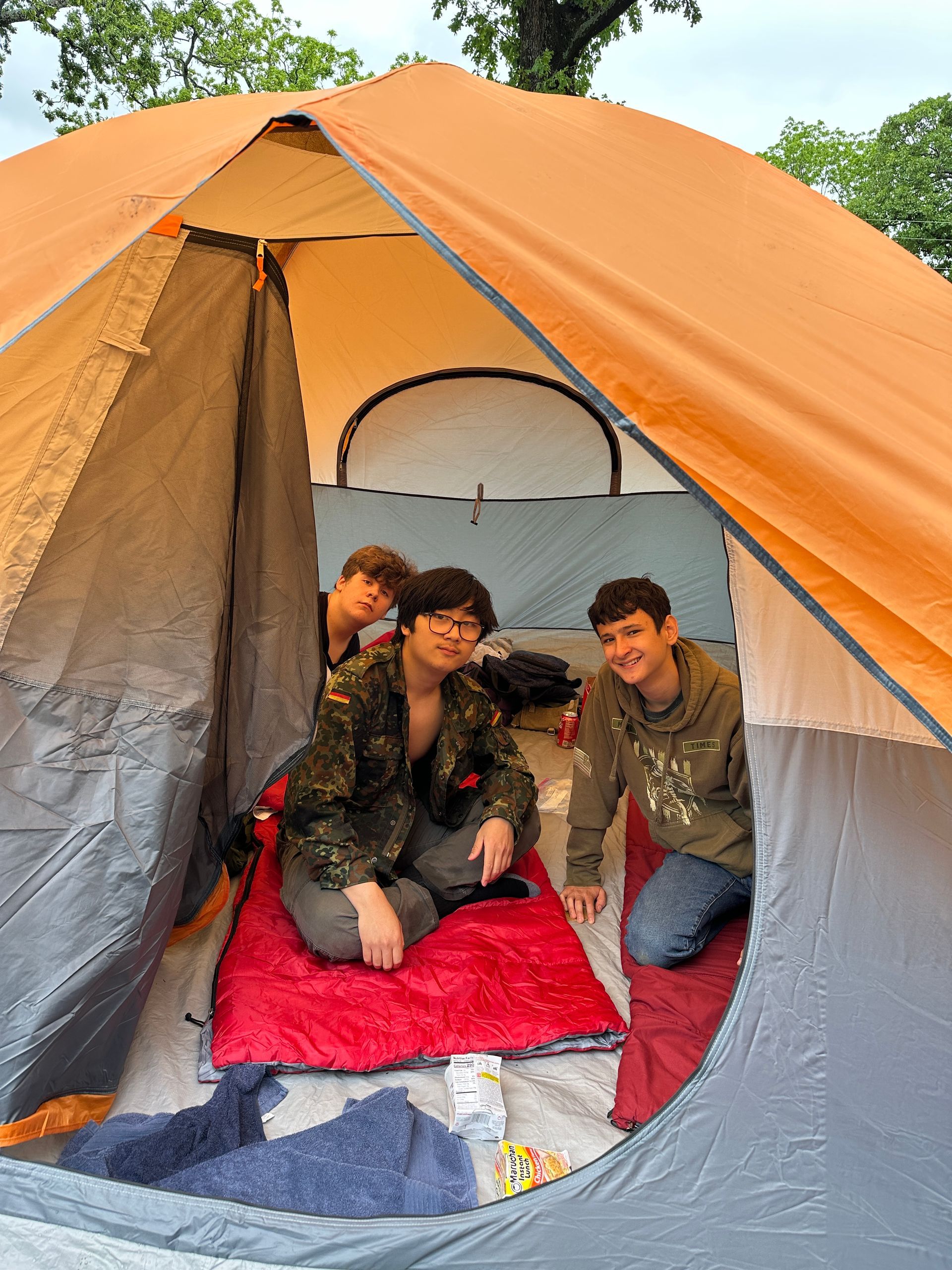 Three people sitting inside an orange and gray camping tent on red blankets