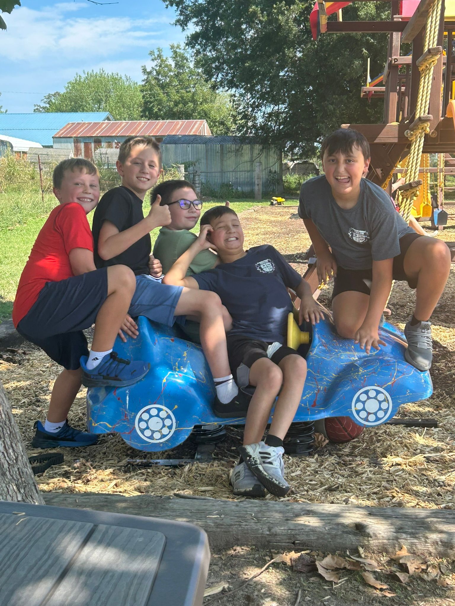 Group of boys on a blue playground car, smiling and posing. Outdoors, sunny day.