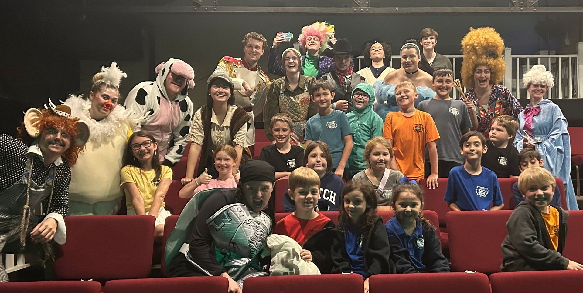Group of people in costumes, likely after a play. Theater stage, red seats.