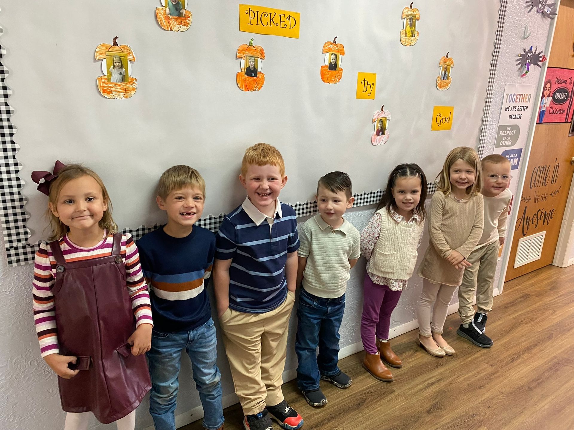 Seven children stand against a wall decorated with apple-shaped cutouts.