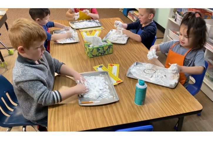 Children playing with shaving cream on trays at a table.