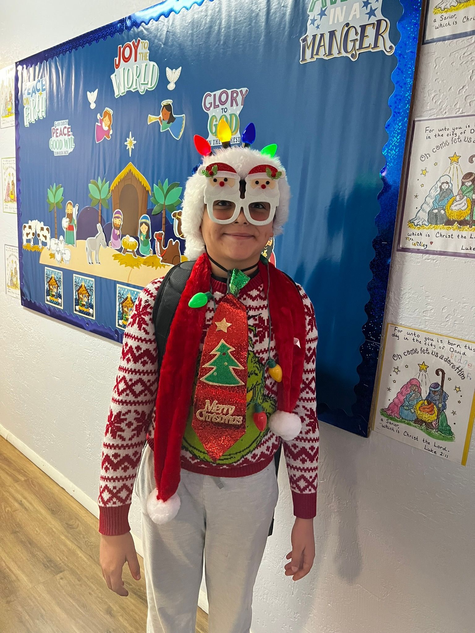 Person in festive Christmas attire, standing in front of a blue backdrop with nativity scene.
