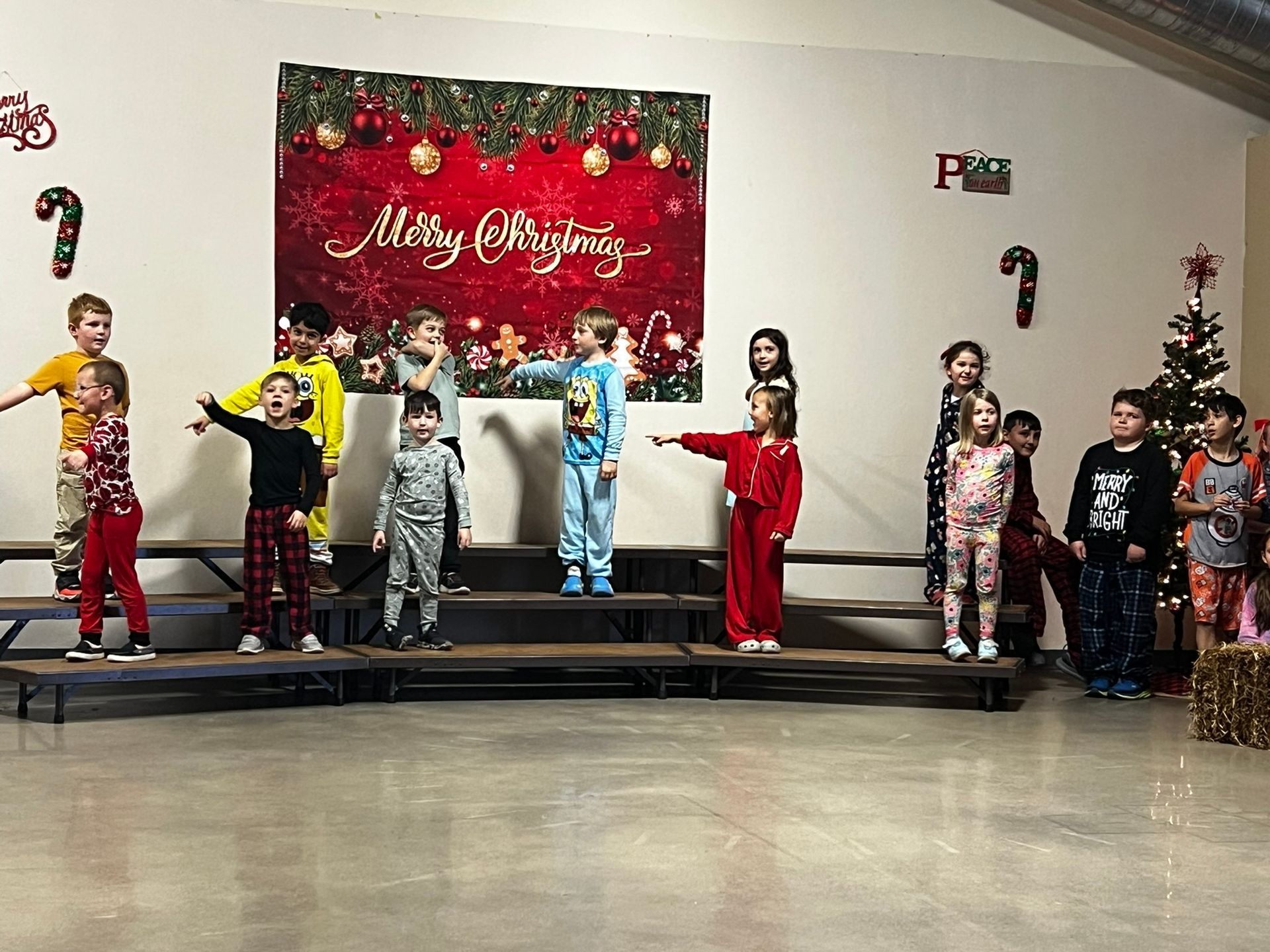 Children in pajamas perform on a stage with Christmas decorations.