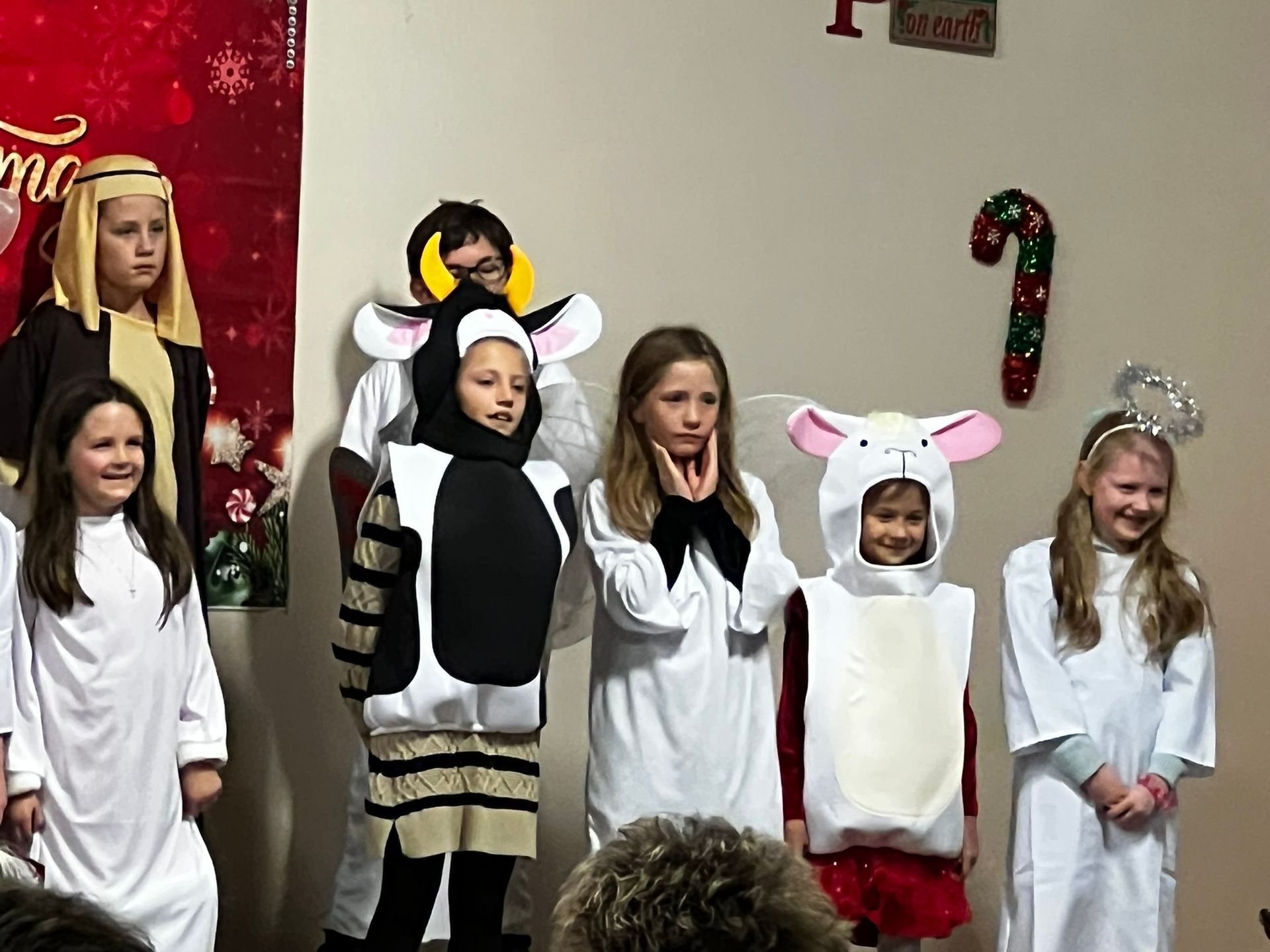 Children in costumes for a Christmas play; shepherds, angel, cow, and sheep on a stage.
