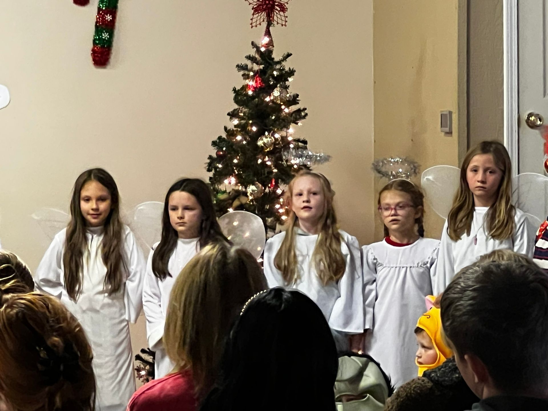 Children dressed as angels performing in front of a Christmas tree.