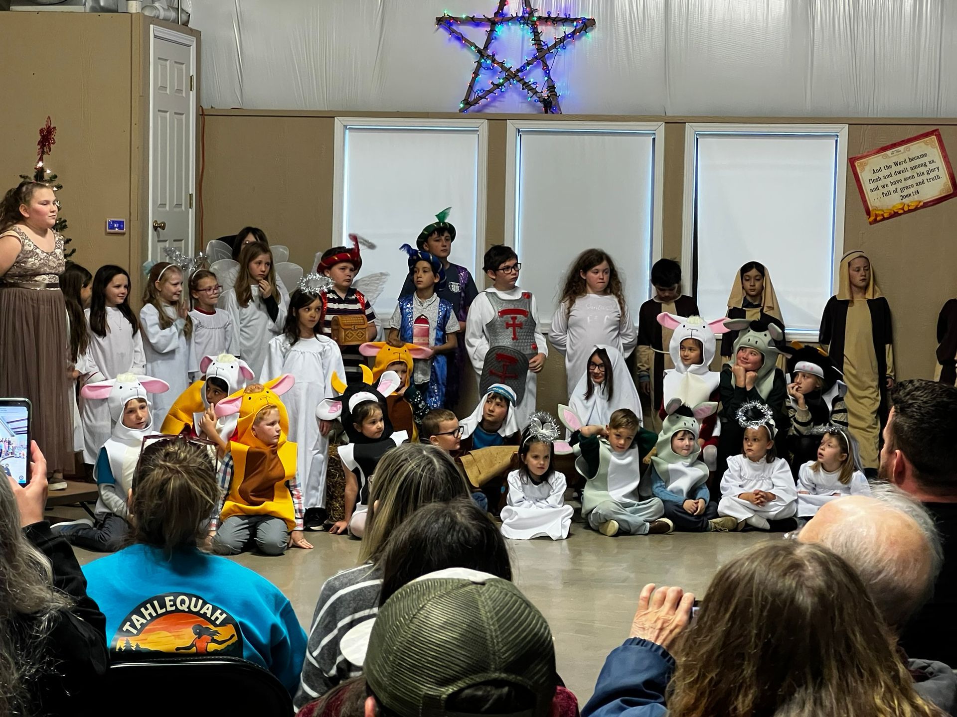 Children in costumes on a stage, performing for an audience; star decoration overhead.
