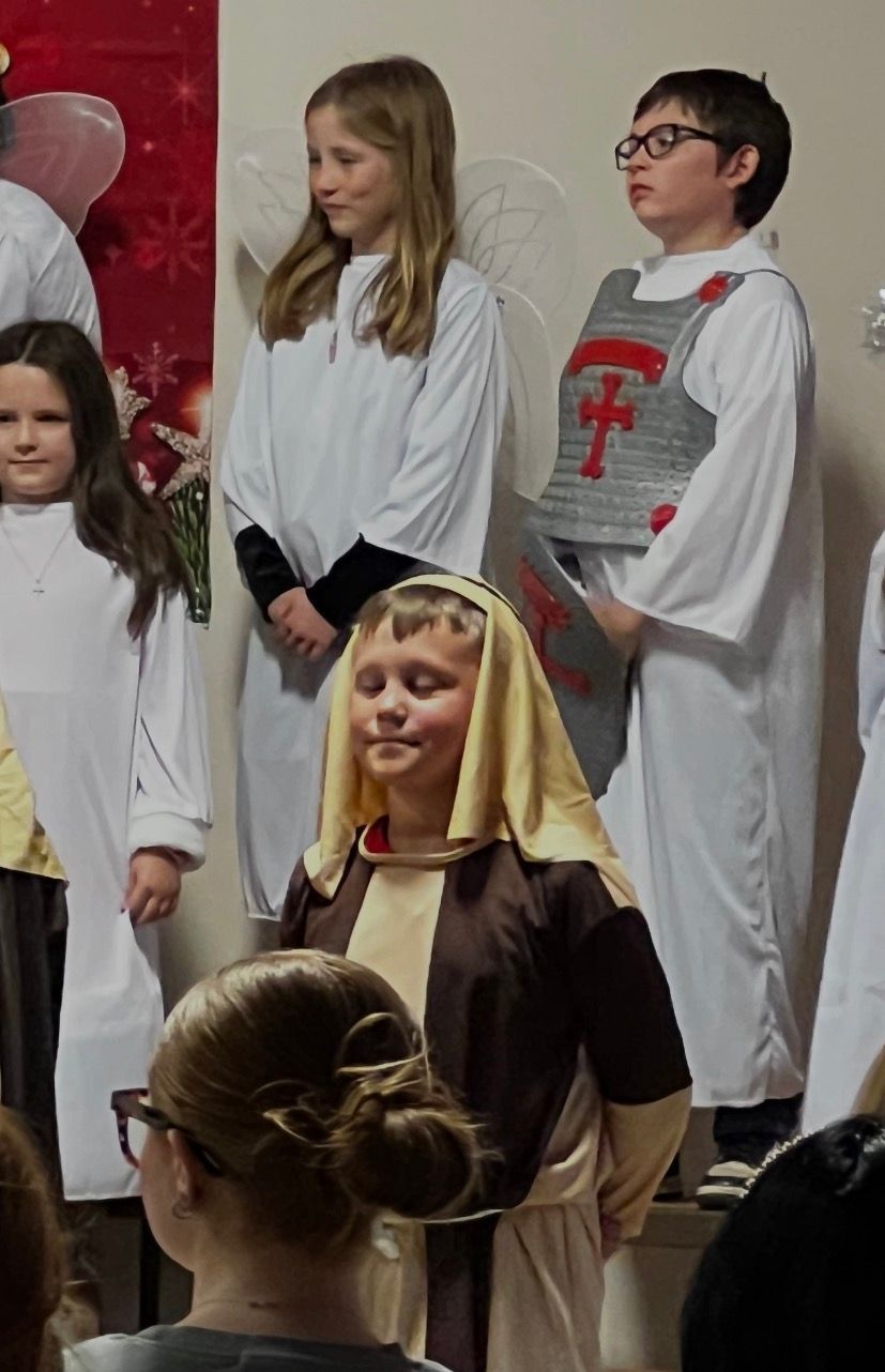 Children in costumes, possibly for a play. One wears a brown robe, another has angel wings, and a third a knight's vest.