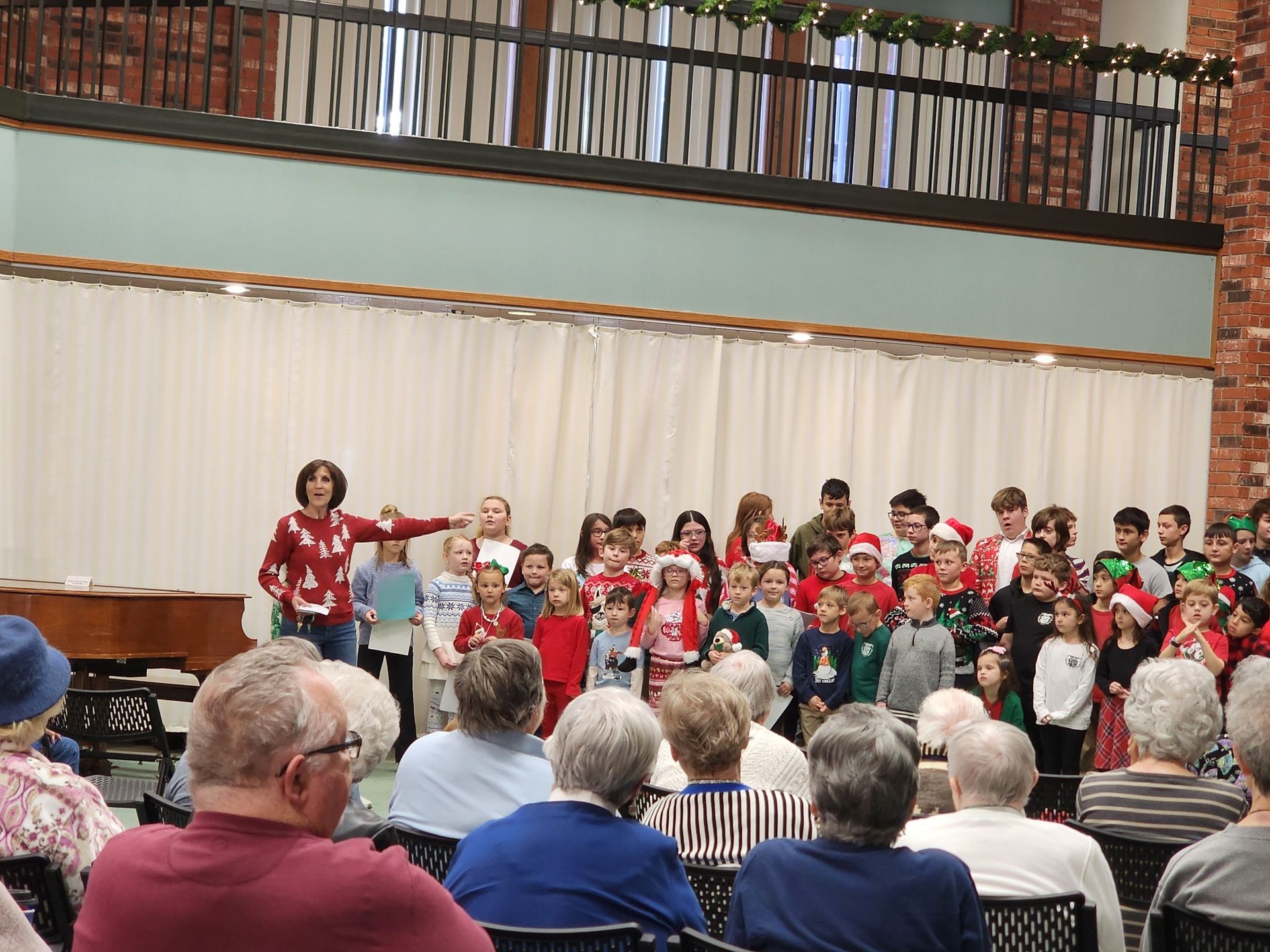 A group of children in holiday attire performing in front of an audience in a hall.
