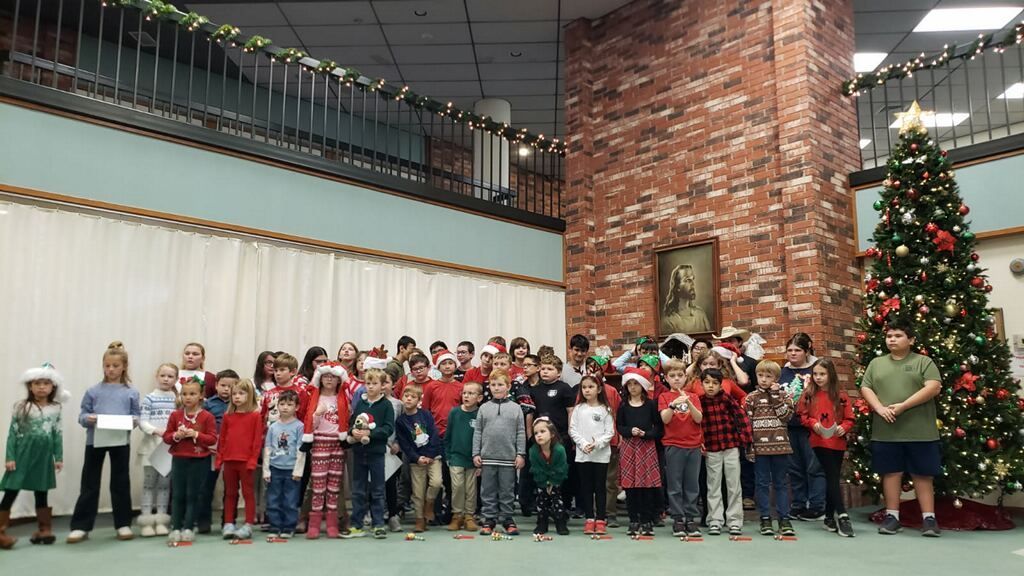 Children in festive attire pose in front of a Christmas tree in a decorated room.