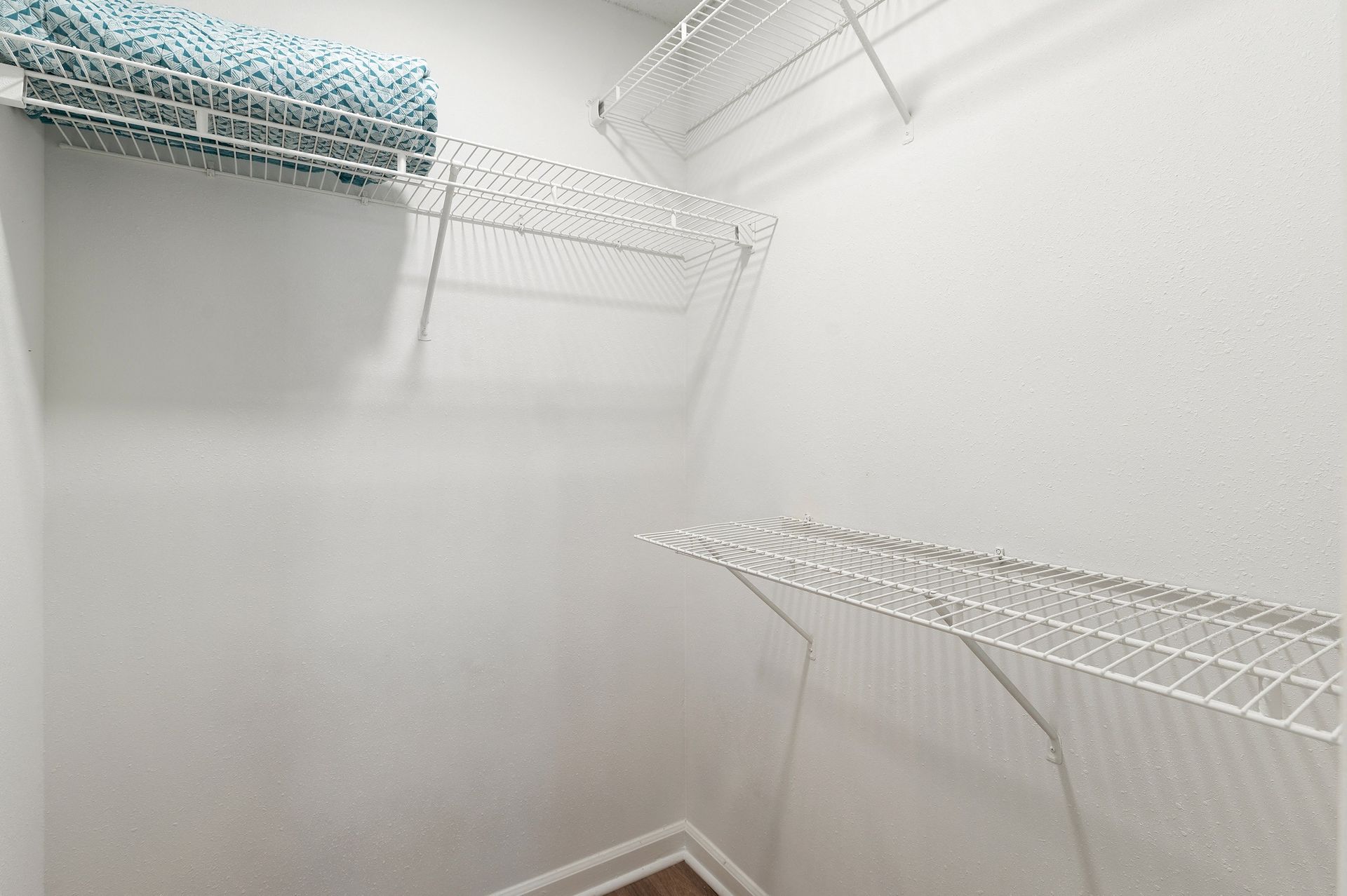 Empty white closet with wire shelves. A blue rolled-up towel is on a top shelf at Creekside at White Oak in Newnan, GA.