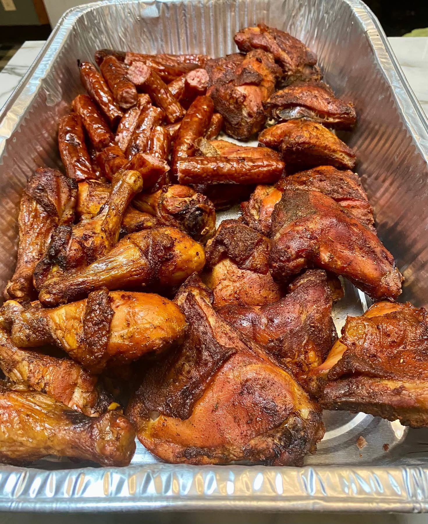 A tray of chicken wings and sausages on a table.