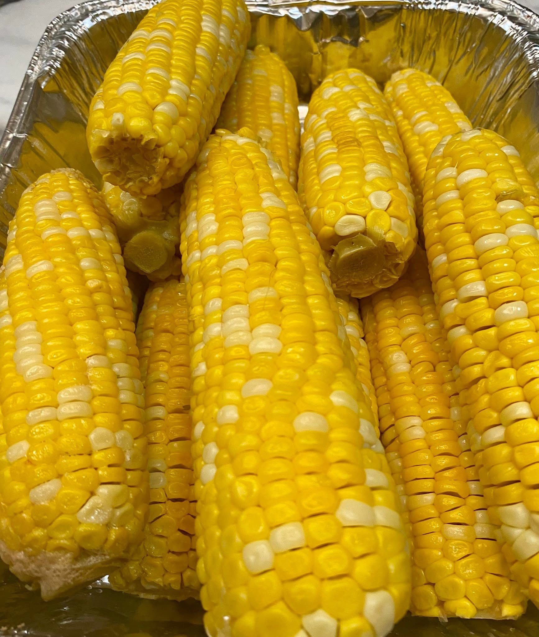 A bunch of corn on the cob in a tin foil container.