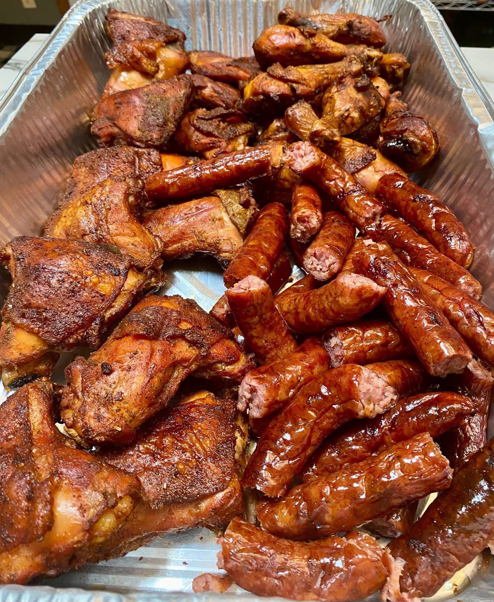 A tray of chicken wings and sausages on a table.