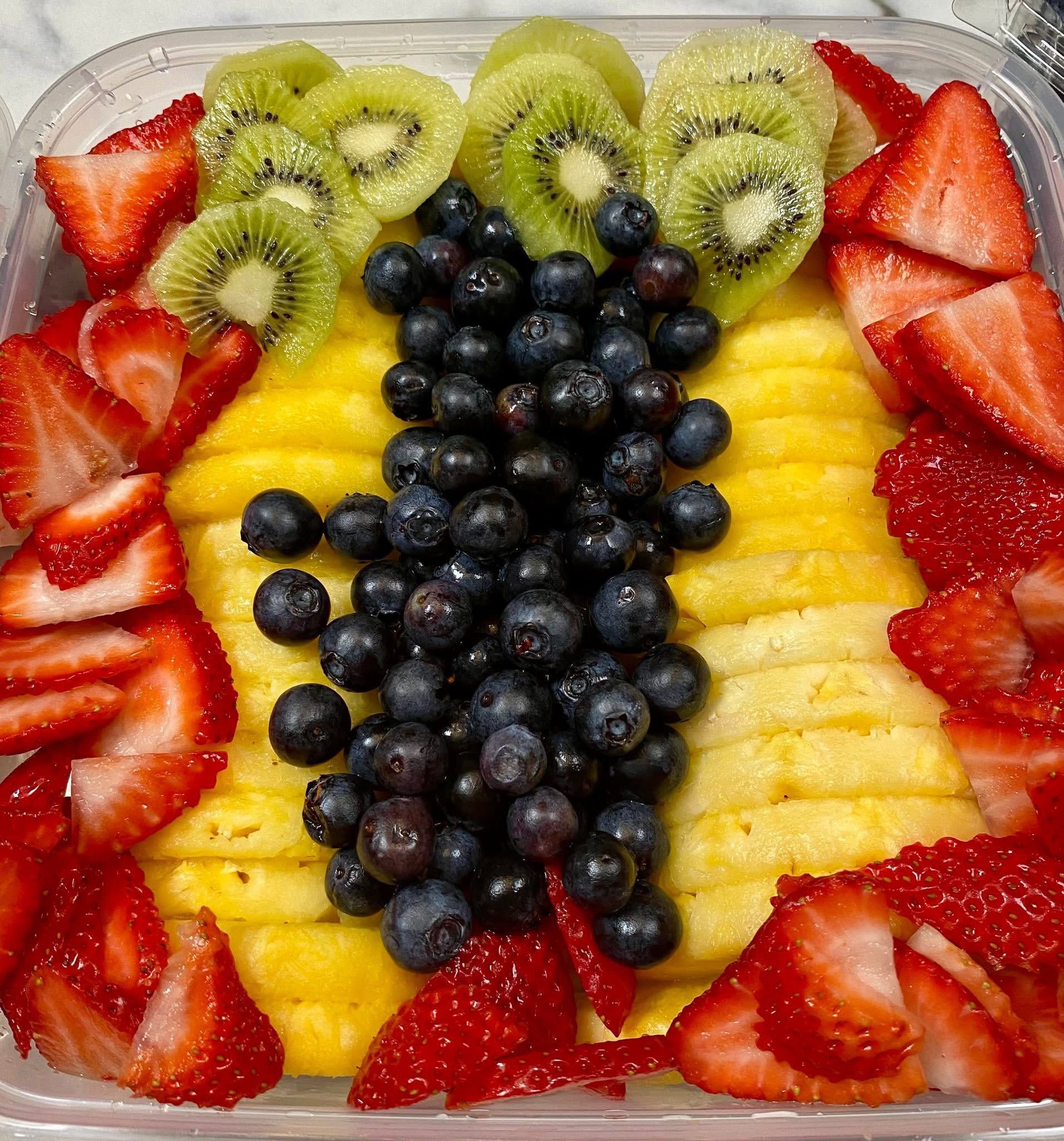 A plastic container filled with pineapple , strawberries , blueberries and kiwi slices.