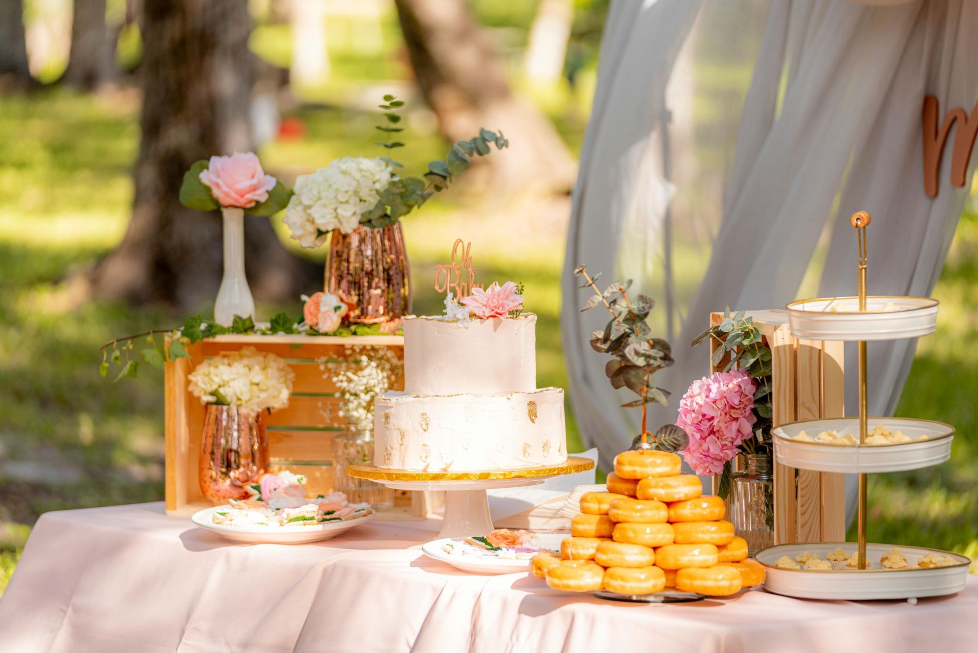 A table with a cake , donuts , and flowers on it.