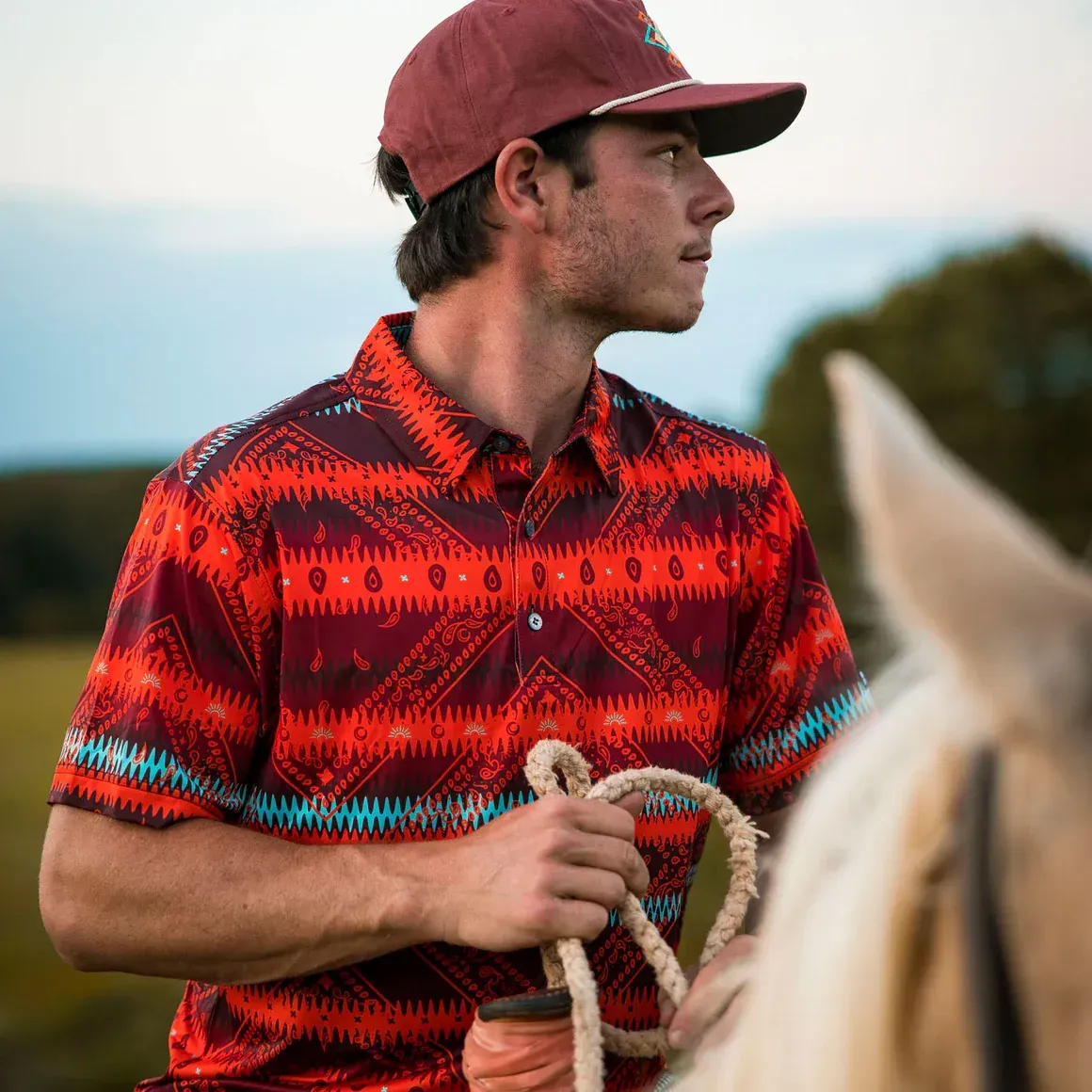 A man wearing a hat and a red shirt is riding a horse