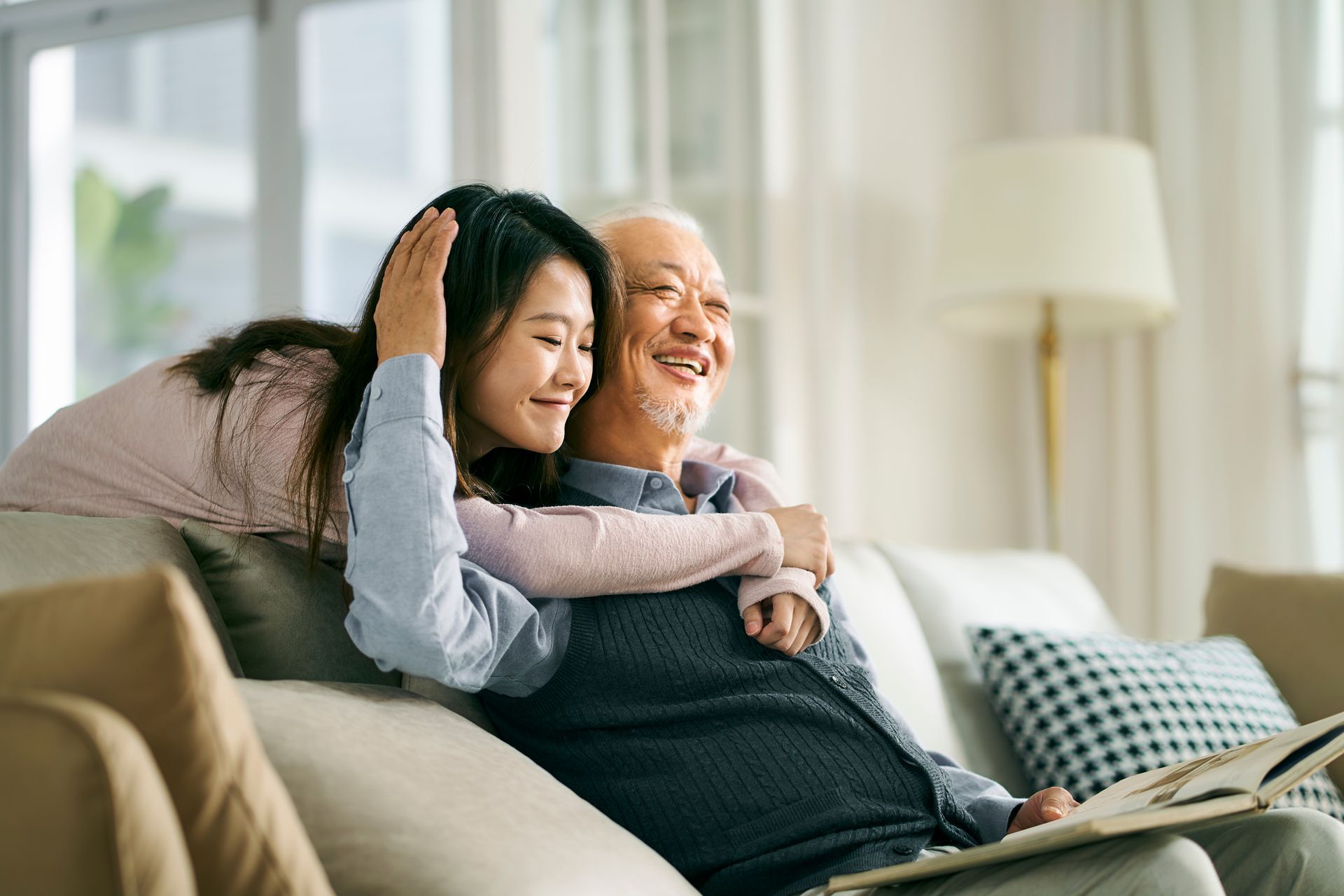 A woman is hugging an older man while they sit on a couch.