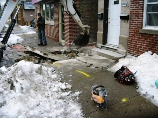 A man is standing in front of a brick building with a shovel in the snow