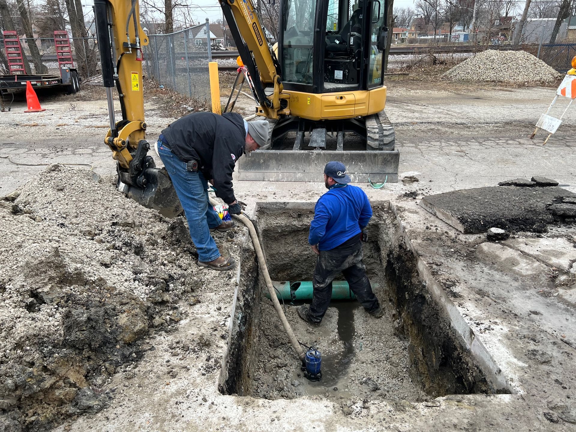 Two men are working on a pipe in a hole in the ground.