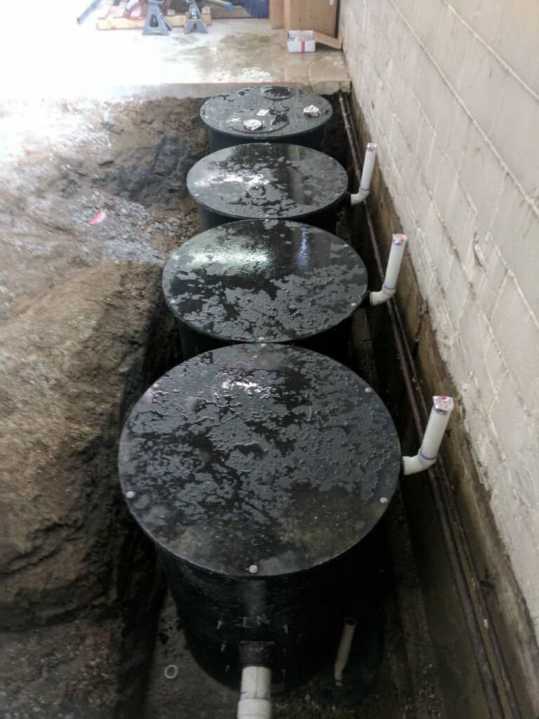 A row of black containers are sitting in the dirt next to a brick wall.
