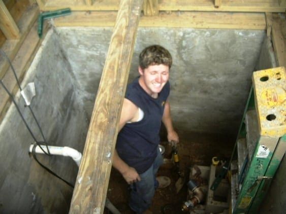 A man is standing in a hole with a ladder next to him