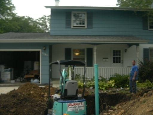 A murphy 's mini excavator is parked in front of a blue house