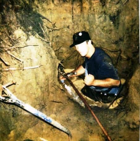 A man is kneeling in the dirt holding a shovel.