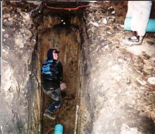A man is standing in a trench next to a pipe