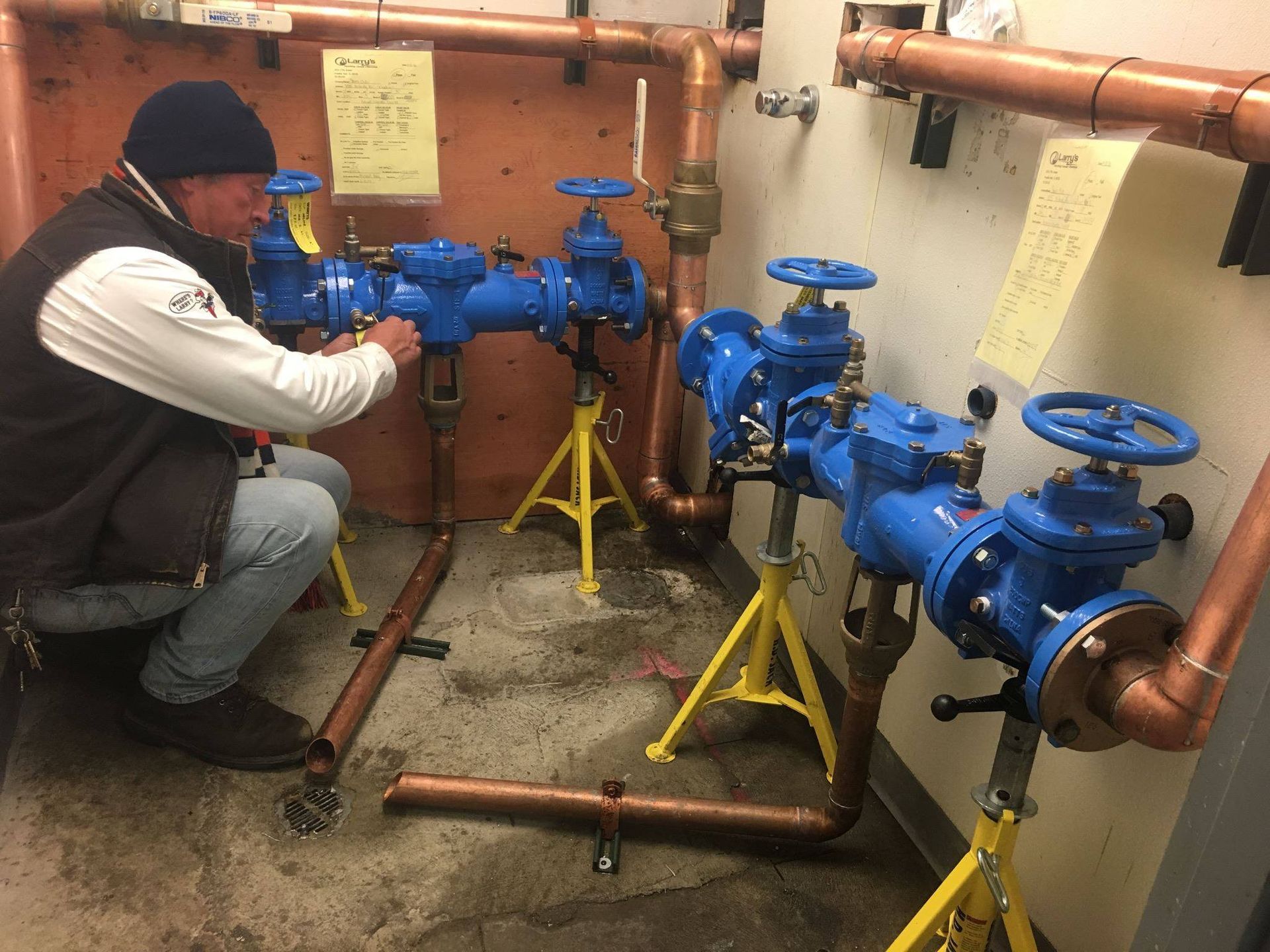A man is kneeling down in a room with pipes and valves.