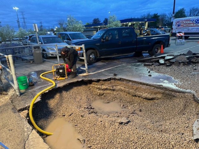 A man is working on a hole in the ground in a parking lot.