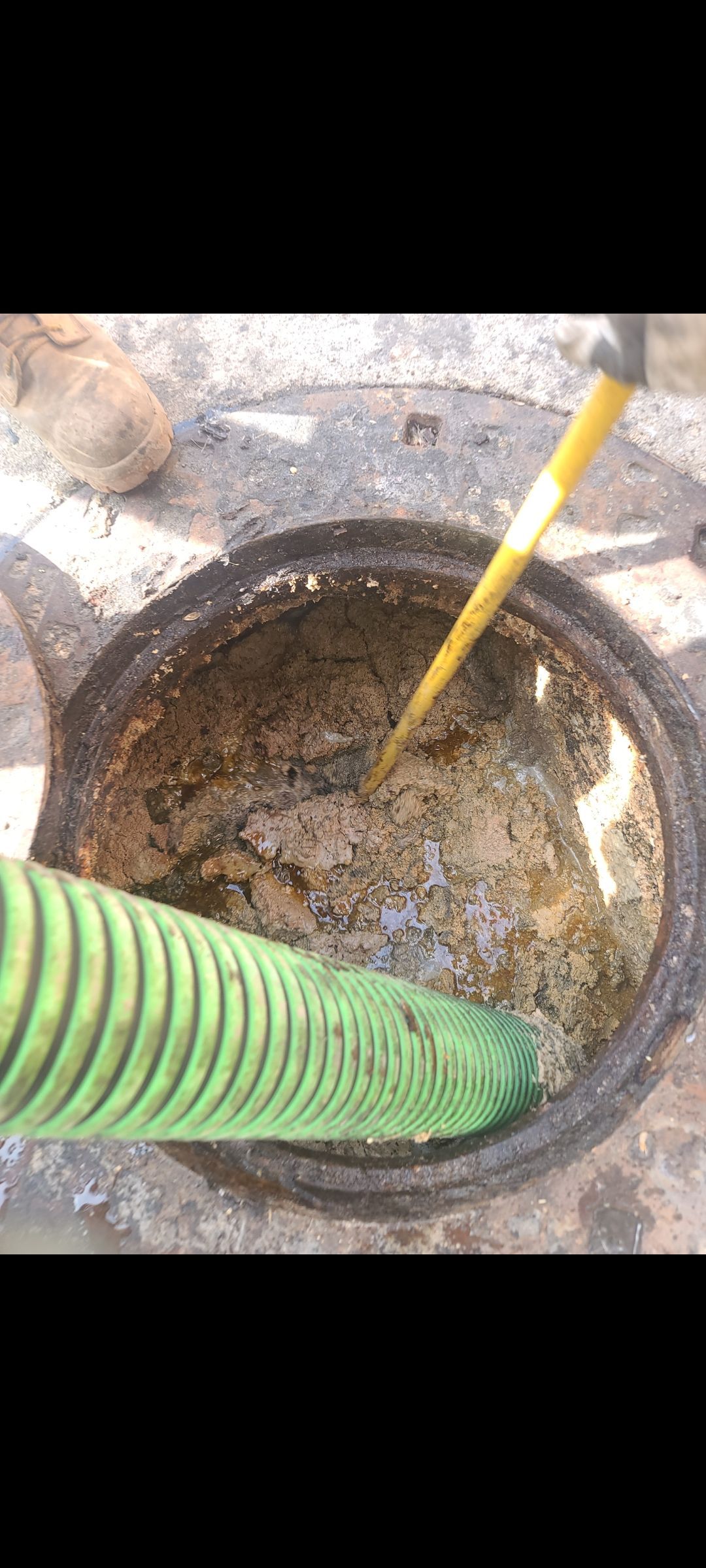 A green hose is being used to clean a manhole cover.