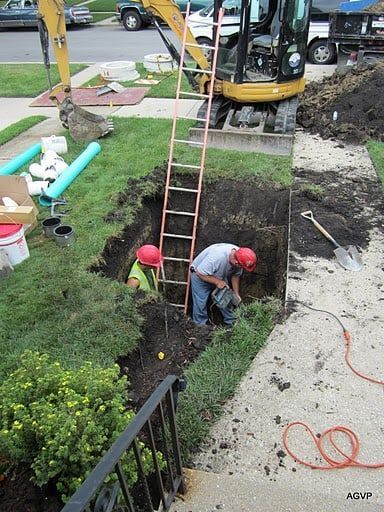 Two construction workers are digging a hole in front of a house