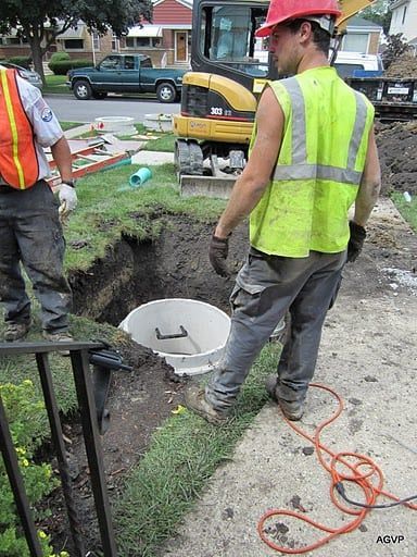 A man wearing a hard hat and a yellow vest is standing next to a hole in the ground.