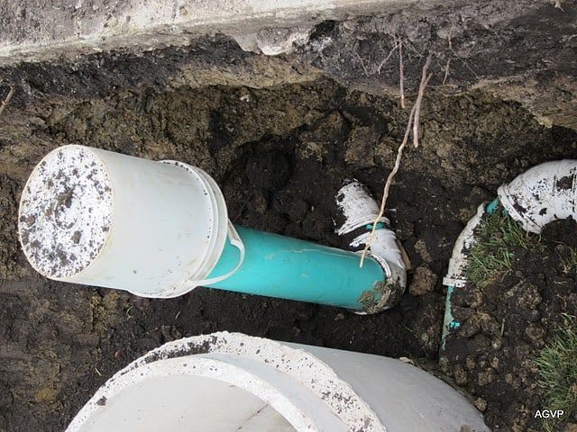 A green pipe is laying in the dirt next to a white pipe.