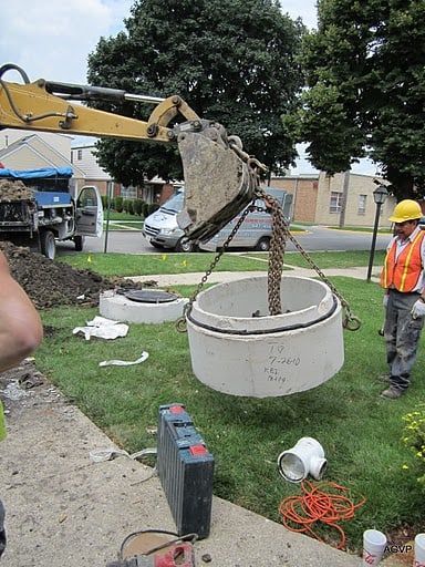 A man is standing next to a manhole cover being lifted by a crane.