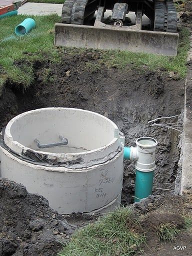 A concrete ring is sitting in the dirt next to a green pipe.
