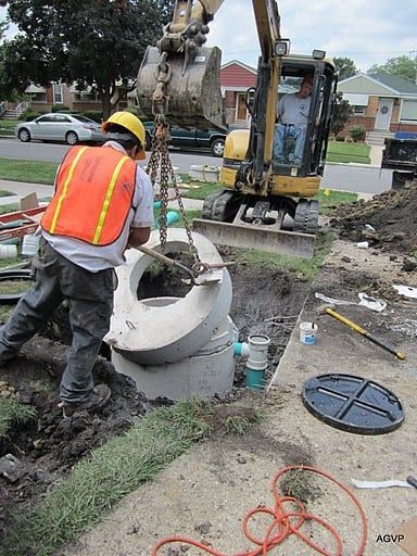 A man in an orange vest is lifting a large concrete object.