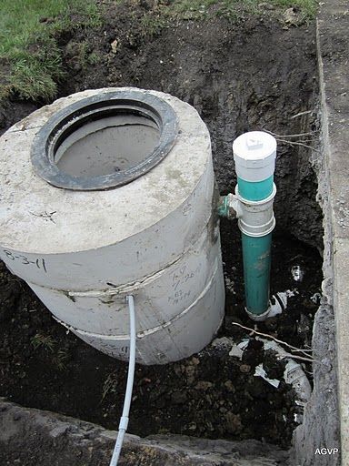 A manhole cover is sitting in the dirt next to a green pipe.