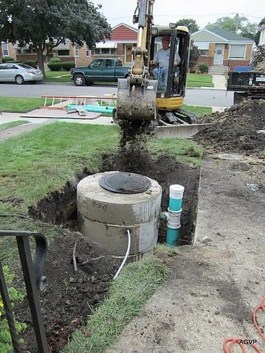 A man is driving a bulldozer in the dirt next to a septic tank.