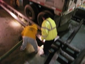 A man in a yellow jacket is kneeling next to a truck.