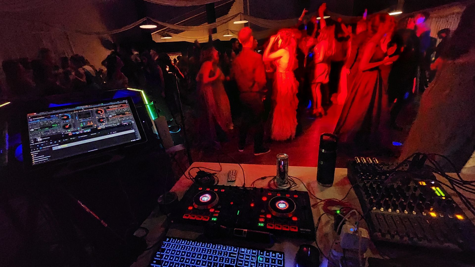 A dj is playing music at a party with people dancing in the background.
