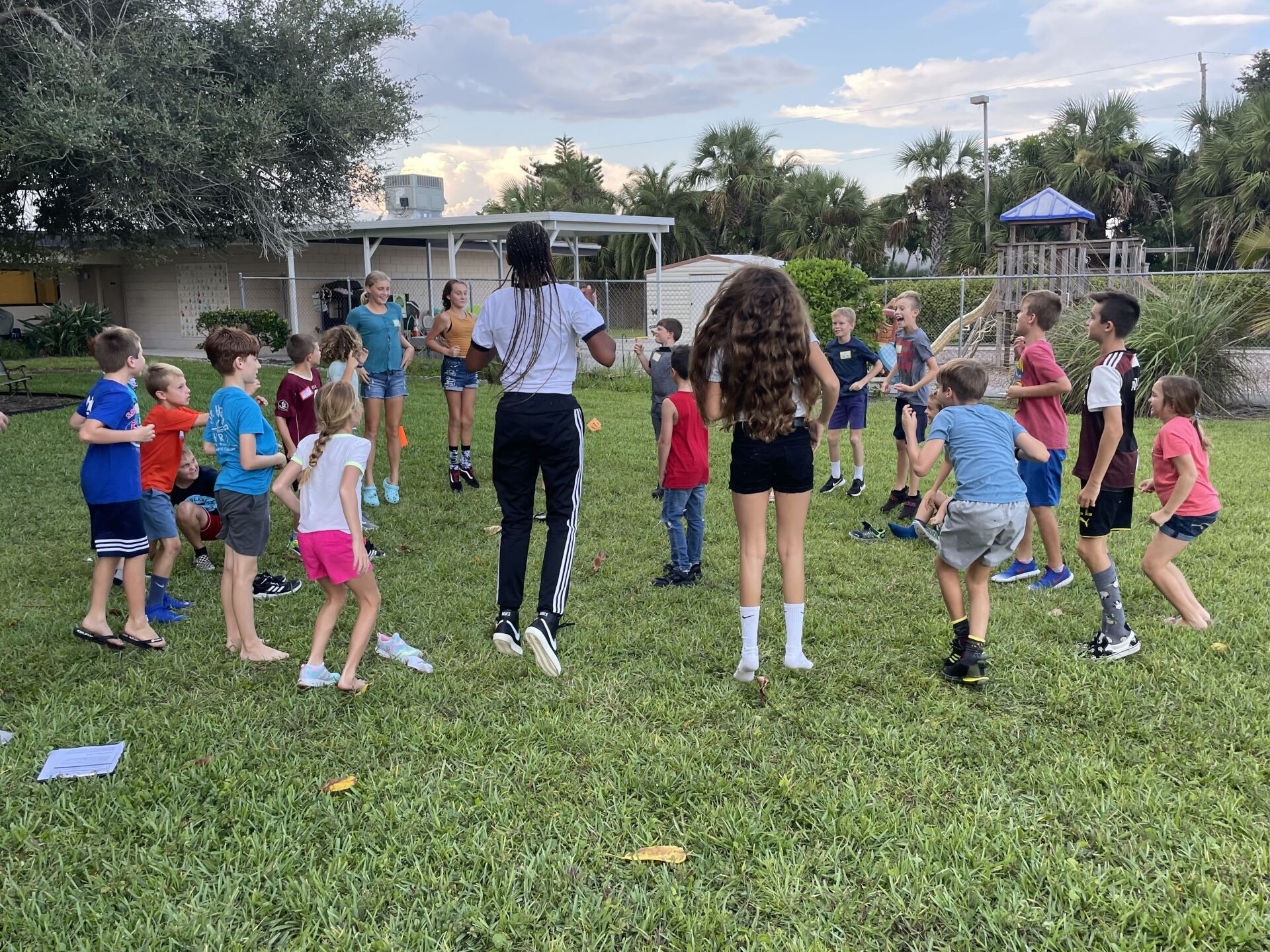 A group of children are standing in a circle in a grassy field.
