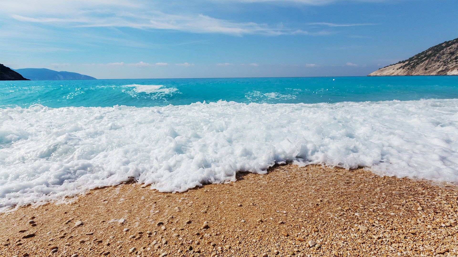 A close up of a beach with waves crashing on the sand.