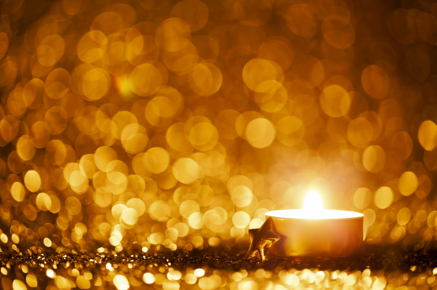 A single candle lit in a dark room - the candle is illuminating the darkness with glitter-like gold